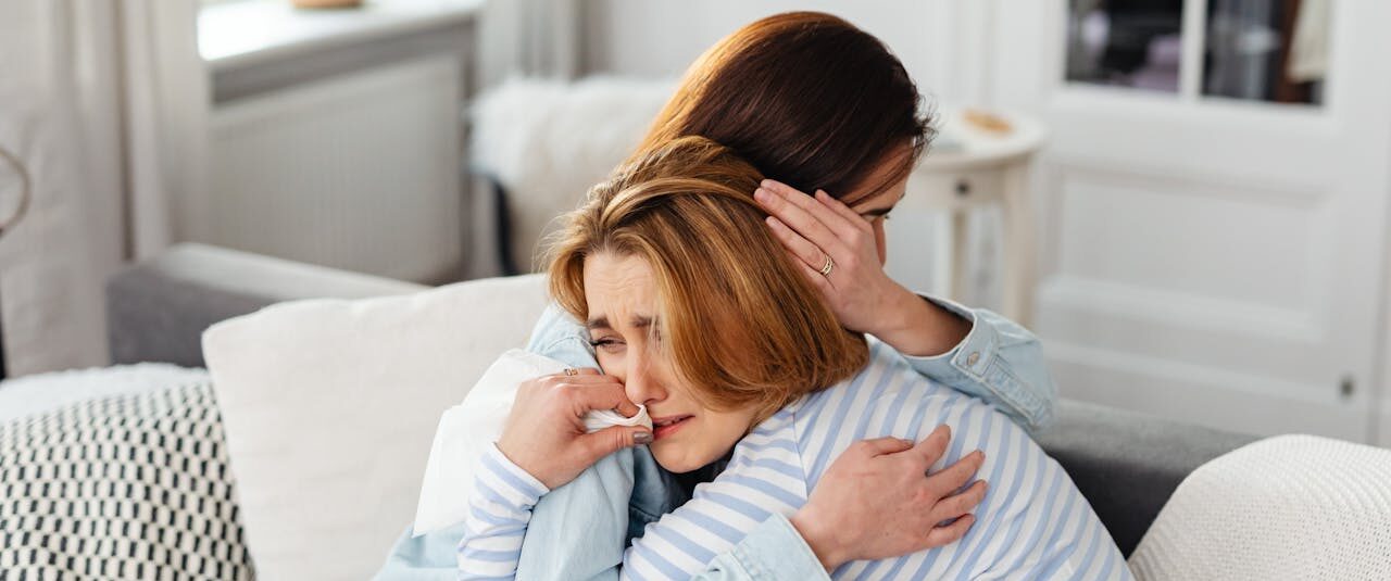 Two women embrace on a couch, conveying emotions of comfort and support indoors.